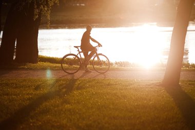 Sağlıklı genç adam bisiklet sürüyor, doğanın ve güneşin tadını çıkarıyor. Özgür bir gezgin gün batımında bir bisikletle seyahat eder. Macera ve seyahat kavramı. Yalnız bisikletçi parkta dinleniyor..