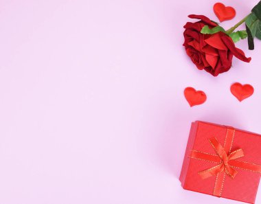 Yapay kırmızı gül tomurcuğu, hediye kutusu ve pembe arka planda iki dekoratif kalp fotokopi alanı. Sevgililer Günü konsepti.