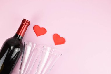 İki bardak, dekoratif kalpler ve pembe arka planda bir şişe şarap..