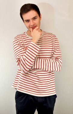 Genç ve çekici bir adam hafif bir gülümsemeyle kameraya bakar. Sağ el çeneye doğru kaldırılır. Görüntü hafif bir arkaplanda çekildi.