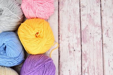 Açık ahşap bir yüzey üzerinde birkaç sıra renkte örgü yünü serilmiş..