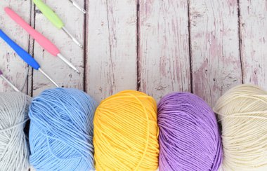 Örgü örmek için renkli yün toplar farklı boyutlarda örgü kancalarının yanına dizilmiş..