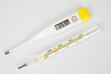 Elektronik ve cıva termometrelerin üst görünümü beyaz arka planda yan yana yatar.