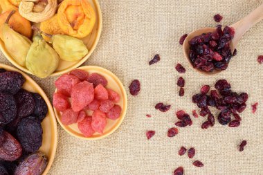 Birkaç tabak kurutulmuş meyve ve masaya saçılmış kurutulmuş yaban mersinli ahşap bir kaşık.