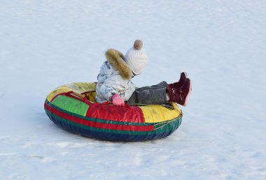 Hafif ceketli küçük bir kız, dağdan şişme bir kar tüpünün üzerinde geliyor.