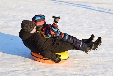 Baba ve oğul dağdan aşağı şişme bir kar tüneline biniyorlar.