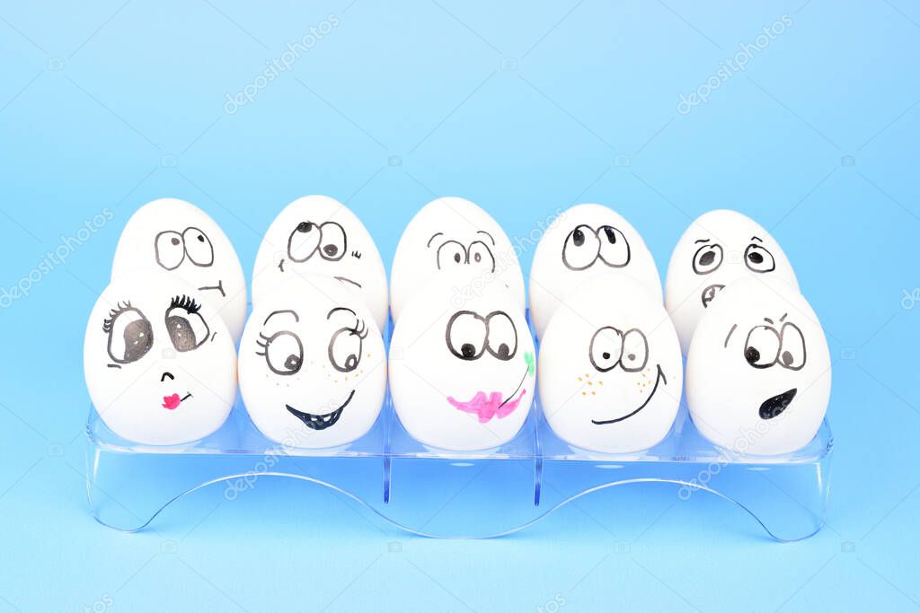 A dozen chicken eggs with painted faces on a plastic stand isolated on a light blue background.