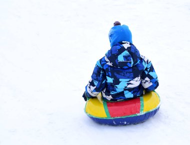 Küçük çocuk kar kaydırağından şişme bir kızakla kayıyor.