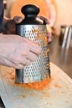 Metal rende havuç rendeleyen kadın elleri. Havuçlar kesme tahtasına dökülüyor..