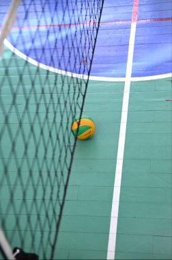 Voleybol sahasında voleybol kalesinin altında. Sahada beyaz ve kırmızı işaretler görülüyor..