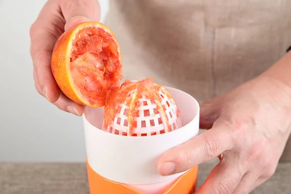 The woman with her right hand holds a half of the orange from which she has just squeezed juice. She holds the hand juicer with her right hand.