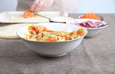 Rendelenmiş lahana, doğranmış bitkiler ve kırmızı dolma biber karışımı. Diğer yemek malzemeleri arka planda görünür..
