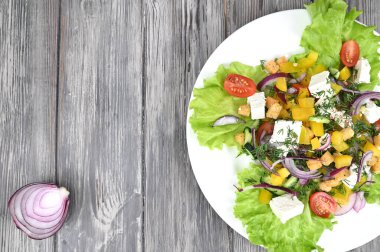 Beyaz tabak ve gri ahşap bir masada Yunan salatası. Yakınlarda bir soğan kafasının yarısı var..
