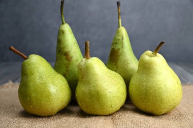 Bir çeşitten üç yeşil armut ve iki tanesi iki sıra yan yana çuval bezinde kalıyor. Çuval bezi ahşap bir yüzeye serilmiştir..