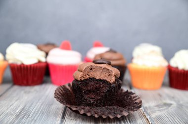 Bir ısırıkla çikolatalı kek. Pasta açık bir kağıt sepetin üzerinde yatıyor. Arka planda diğer kekler görünür..