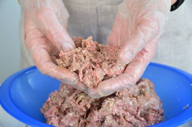 Şeffaf eldivenli bir kadın kıyma etlerini ayırıyor, kemiklerin kalıntılarını ayırıyor. Kıyma, mavi plastik bir kasede..
