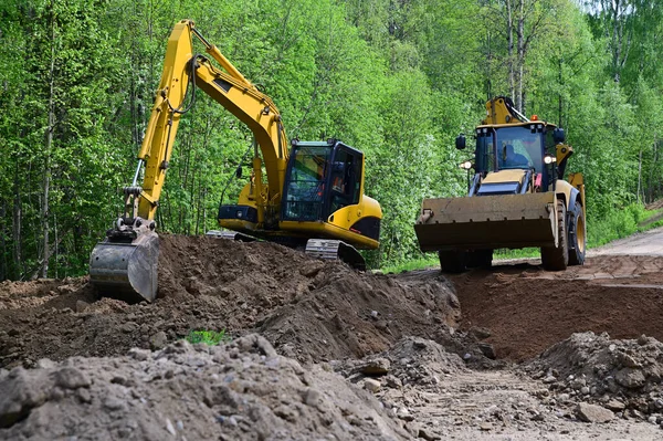 Kazıcı ve buldozer köy yolunda çalışıyor. Toprak bir yolda yol makineleri.
