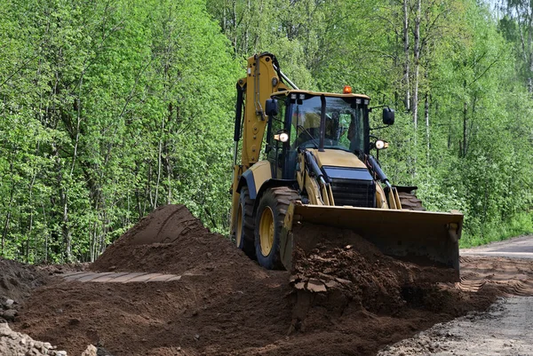 Kır yolundaki kum yığınlarını dümdüz eden buldozer. Yol ağır makineleri toprak bir yolda çalışır..