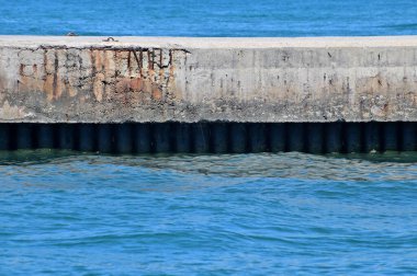 Demir yığınlarının görünür olduğu zeminde güçlendirilmiş beton bir ranzanın parçası. Dalgakıranın önünde ve arkasında mavi deniz.
