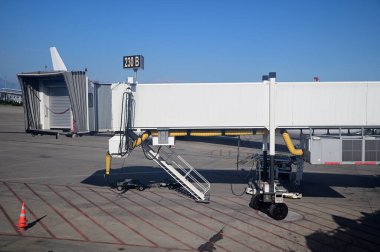 Büyük bir havaalanındaki uçağa binen yolcular için bir kol. Arka planda parlak mavi gökyüzü var.