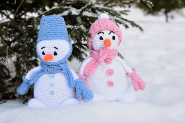 İki örülmüş kardan adam ağacın altında karların üzerinde duruyor. Birinin mavi, diğerinin pembe elbiseleri var..