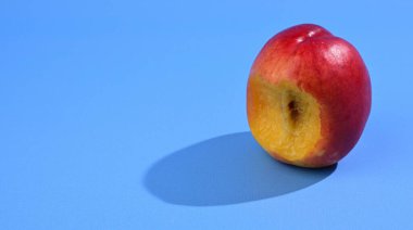 Nektarini görünür bir tohumla ısırdı ve koyu bir gölgeyle, açık mavi arka planda izole etti..