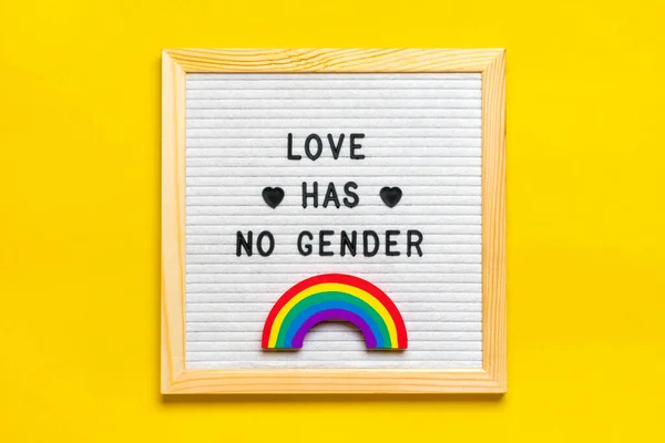 Felt board with quote, wooden hands holds rainbow with colors of LGBT isolated on yellow background Top view Flat lay Pride month concept.