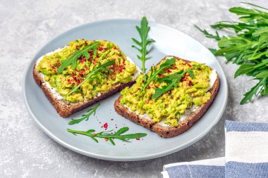 Kahvaltı için sandviç hazırla - bir dilim kepekli ekmek, krem peynir, guakomole, roka ile süslenmiş, beton masa üzerinde kırmızı biber düz konsept ev yapımı gıda konsepti.