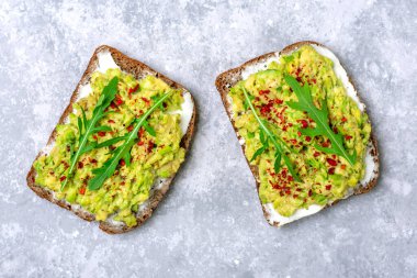 Kahvaltı için sandviç hazırla - bir dilim kepekli ekmek, krem peynir, guakomole, roka ile süslenmiş, beton masa üzerinde kırmızı biber düz konsept ev yapımı gıda konsepti.