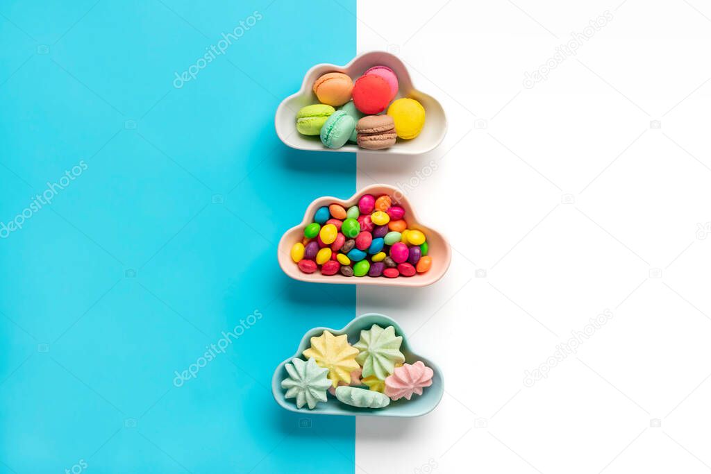 colorful candies - lollipops, meringues, macaroon in bowl in shape of cloud isolated on blue, white background Flat lay Top View Knolling Unhealthy and tasty food creative concept Holiday card.