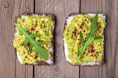 Kahvaltı için sandviçler hazırla - bir dilim kepekli ekmek, krem peynir, guakomole, roka ile süslenmiş, ahşap masa üzerinde kırmızı biber düz görünüm ev yapımı gıda konsepti