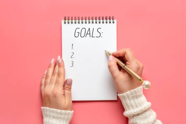 Kadın eli kalemle yeni yıl 2021 hedeflerini beyaz not defteri, kaktüs, pembe arka planda mum düz görünüm iş motivasyonu, fikir, başarı, vizyon, ilham kavramı üzerine yazıyor.