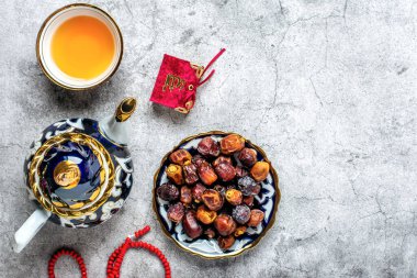 İftar sırasında popüler yiyecekler - macadamia fındığı, şam fıstığı, ceviz, kuru hurma. Karan, tespih, çaydanlık, çimento arkaplanlı siyah çay Üst Manzara Müslüman bayramında kutsal Ramazan ayı uzanıyor.