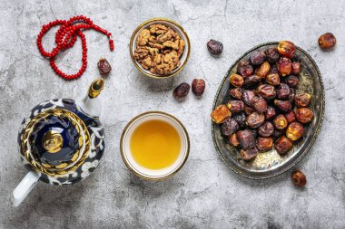 İftar sırasında popüler yiyecekler - macadamia fındığı, şam fıstığı, ceviz, kuru hurma. Karan, tespih, çaydanlık, çimento arkaplanlı siyah çay Üst Manzara Müslüman bayramında kutsal Ramazan ayı uzanıyor.