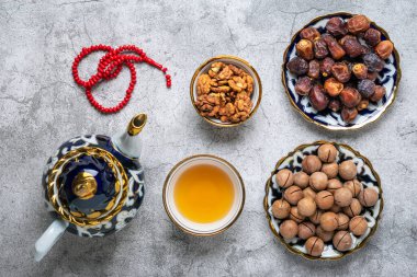 İftar sırasında popüler yiyecekler - macadamia fındığı, şam fıstığı, ceviz, kuru hurma. Karan, tespih, çaydanlık, çimento arkaplanlı siyah çay Üst Manzara Müslüman bayramında kutsal Ramazan ayı uzanıyor