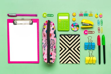 Ofis malzemelerinden çerçeve ataç, makas, kalem, keçeli kalem, bileyici, sırt çantası, hesap makinesi, zımba yeşil arka planda izole edilmiş düz zemin okula geri dön, eğitim kavramı