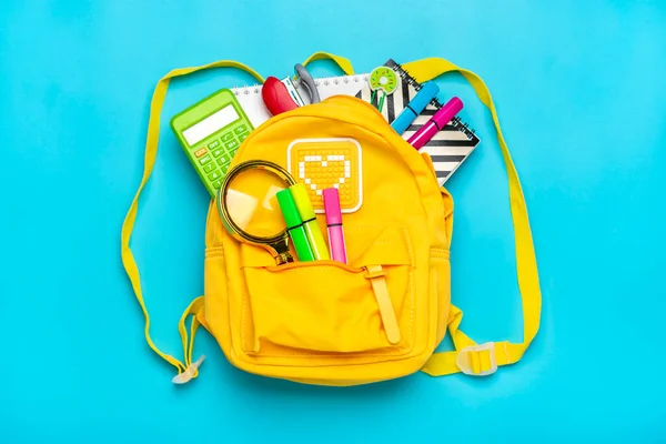 Назад в школу, концепция образования. Желтый рюкзак со школьными принадлежностями - ноутбук, ручки, линейка, калькулятор, ножницы изолированы на синем фоне. Вид сверху. Копирование пространства Плоская композиция — стоковое фото