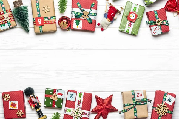 Ručně balené červené, zelené dárkové krabice zdobené stuhami, sněhové vločky a čísla, vánoční ozdoby a dekorace na bílém stole vánoční adventní kalendář koncept Top view Flat lay Dovolenková karta — Stock fotografie