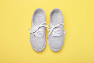 Sarı arka planda bağcıklı gri spor ayakkabılar..