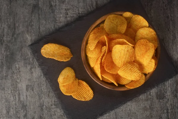 Aardappelchips met kruiden in schaal op een donkere achtergrond, bovenaanzicht. Fast food — Stockfoto