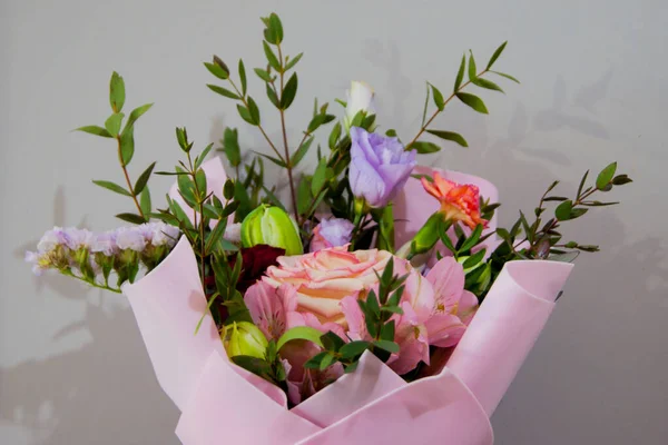 Jemná kytice různých květin v světle růžové obal stojí na šedém pozadí. — Stock fotografie