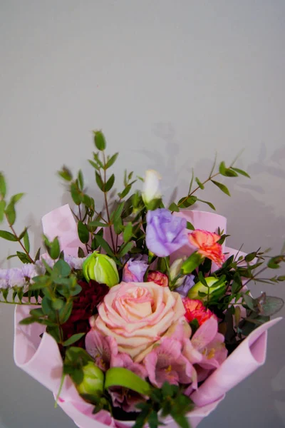 Bouquet délicat de différentes fleurs dans un emballage rose clair sur un fond gris. — Photo
