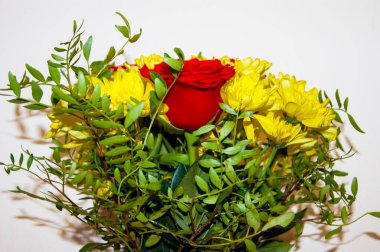 Kırmızı güllerden ve sarı kasımpatılardan yapılmış bir buket çiçek beyaz duvara karşı duran bir vazoda duruyor. Çiçekler büyük. Bir hediye, bir aşk ilanı. Tatil.