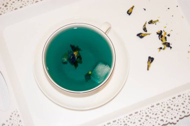 Ruh hali rengi mavi. Beyaz bir fincan çay bardağındaki mavi çay. Beyaz bir fincan tabağı ve beyaz bir tepside duruyor. Yararlı içkiler, iyileştirici özellikler. Beden eğitimi. Çay partisi..