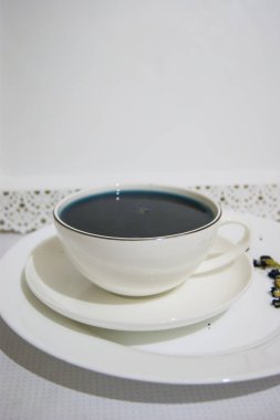 Ruh hali rengi mavi. Beyaz bir fincan çay bardağındaki mavi çay. Beyaz bir fincan tabağı ve beyaz bir tepside duruyor. Yararlı içkiler, iyileştirici özellikler. Beden eğitimi. Çay partisi..