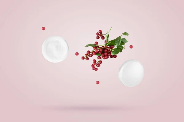 Açık bir kozmetik krem kavanozu ve bir demet küçük kırmızı dut pembe arka planda serbestçe havada süzülüyor. Yükselme kavramı, kozmetik ürünler için doğal malzemeler.