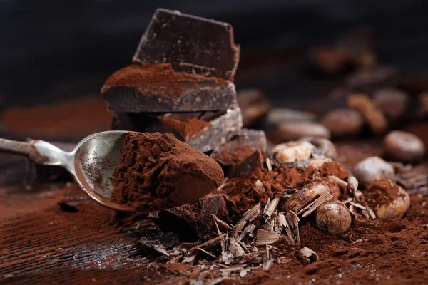 Pedaços de chocolate escuro e cacau em pó em uma mesa de madeira — Fotografia de Stock