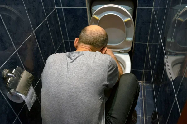 The man is kneeling and fixing the toilet in the home bathroom. Horizontal photo