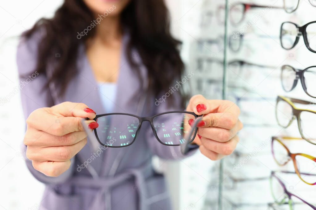 Female hands hold black-framed glasses next to an optics showcase