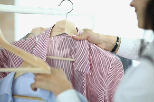 Mujer despega y sostiene en sus manos perchas con camisas —  Fotos de Stock